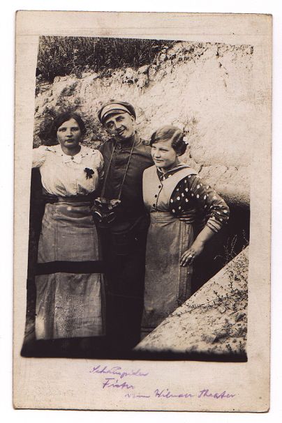 A man stands at the entrance to a sunken building, his arms around the waists of the two young women flanking him.  He is pulling a comic face.