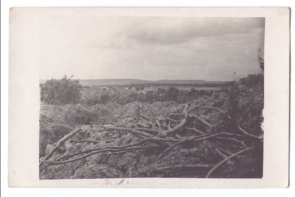 Another battle-scarred landscape. Craters and debris fill the foreground, and a ruined village can be seen on a ridge in the distance.