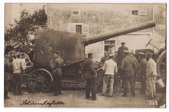 Large cannon with a metal housing mounted on a bogey with wheels, and linked to a tractor.