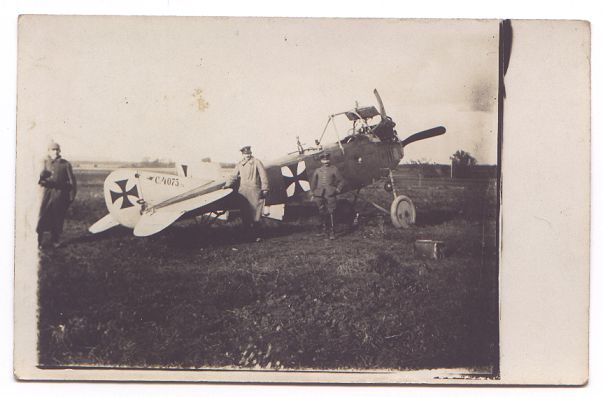 No wings, but they're all OK. Pilot and gunner stand in front of their aeroplane.  The wings are missing, and the propeller is buckled, but otherwise it shows little damage.