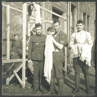 Several men stand round a wash stand outside a stone building. Possibly at training base?