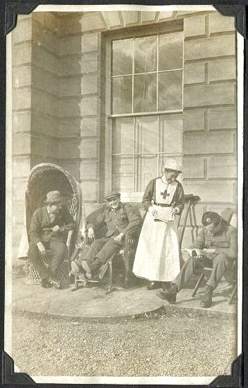 Lady Sybil Grey, wearing a nursing uniform, standing on a terrace with servicemen seated on either side.