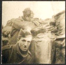 One soldier aims his rifle through a gap in the breastworks, while another turns to look at the camera. 